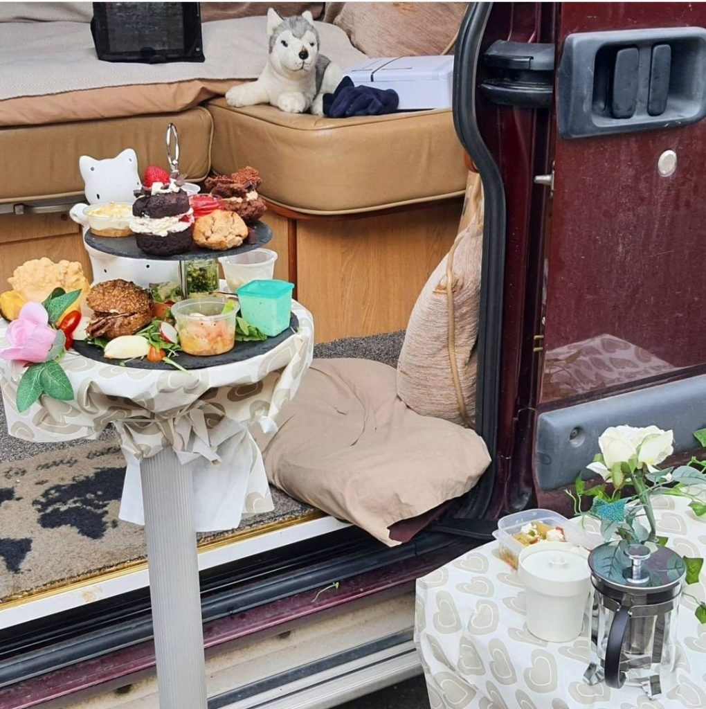 Afternoon tea presented on a table outside a campervan.
There is a toy husky in the background