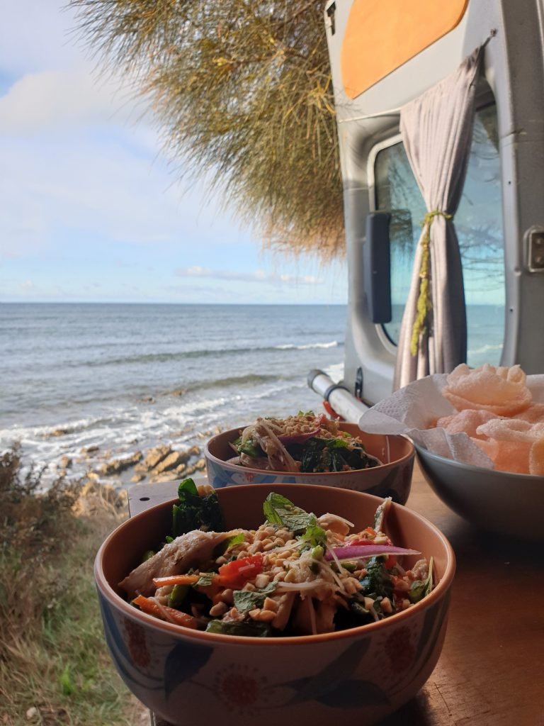 Two bowls of food on a table in the back of the van. The van doors are open and the sea can be seen.