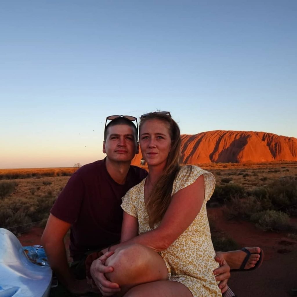 Sarahkai and Sam sitting together in the desert with the sun setting behind them.