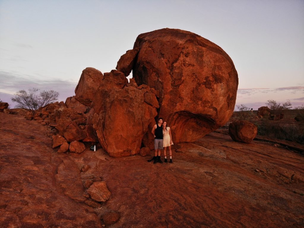 Sarahkai and Sam stood in front of a large red rock in the desert.