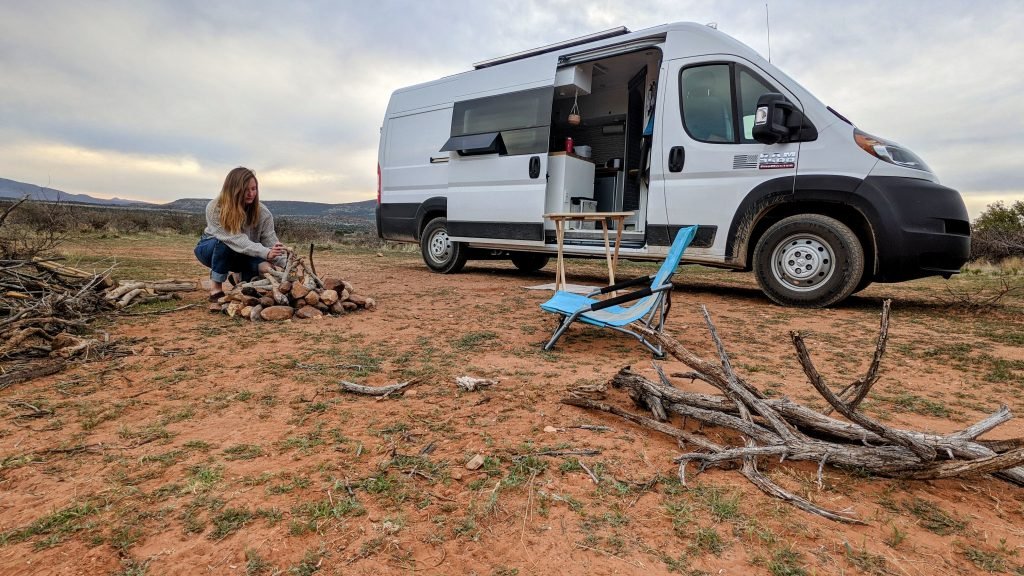 Girl in front of white campervan lighting a campfire