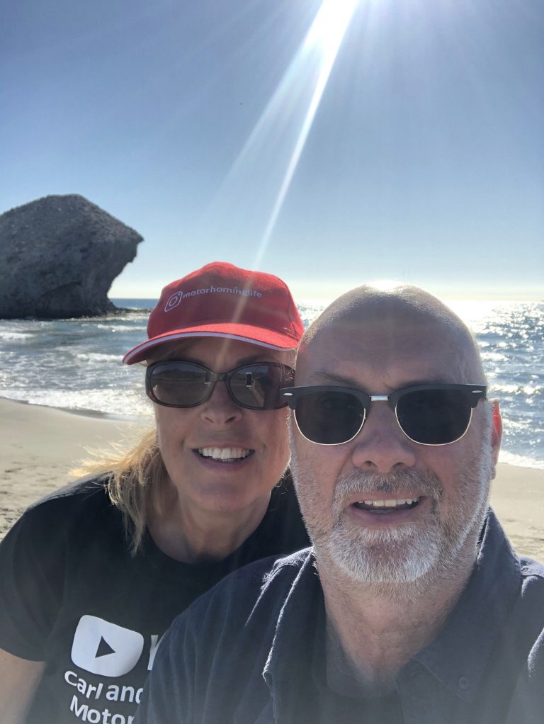 Carl and Sally-Anne are stood together facing the camera with the sea and sun behind them.