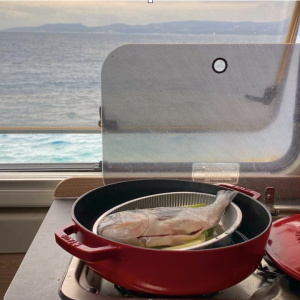 meal cooking on a stove in a campervan. There is a view of the sea through the window