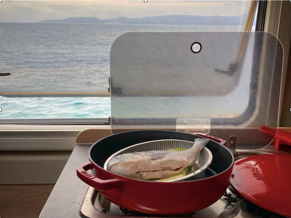 meal cooking on a stove in a campervan. There is a view of the sea through the window