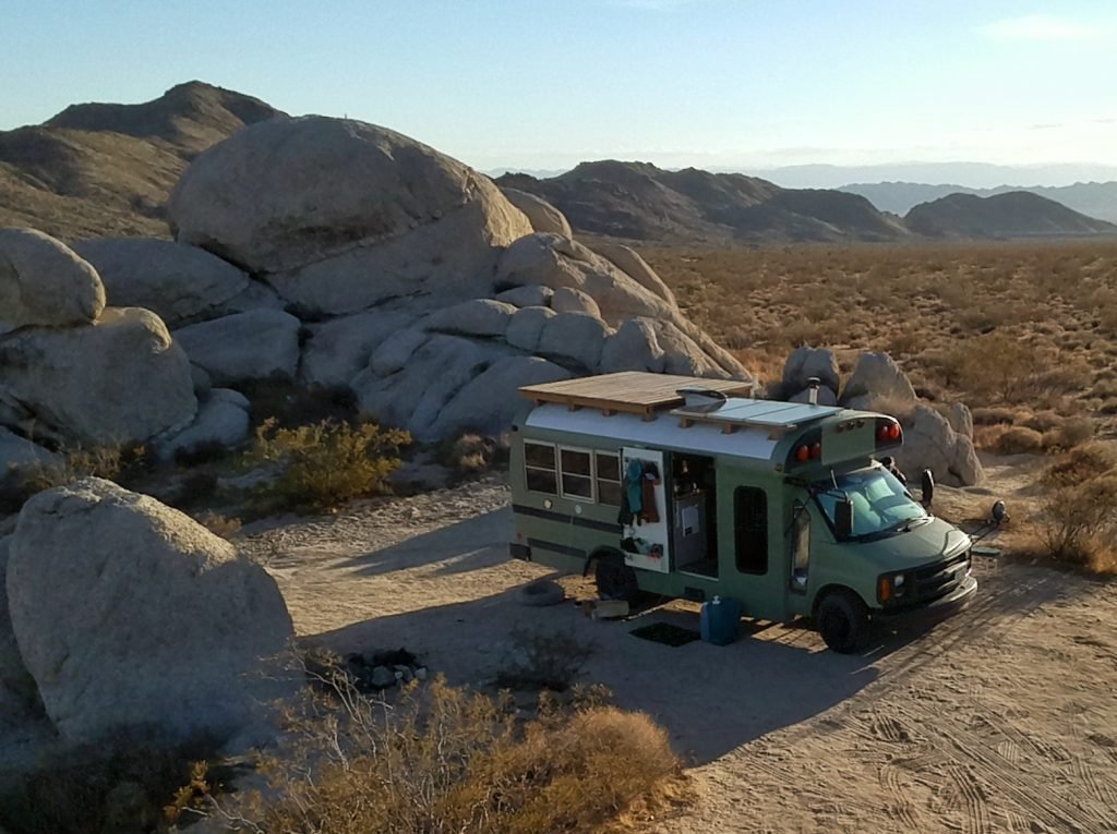 The bus is parked up in the middle of the desert with the doors open