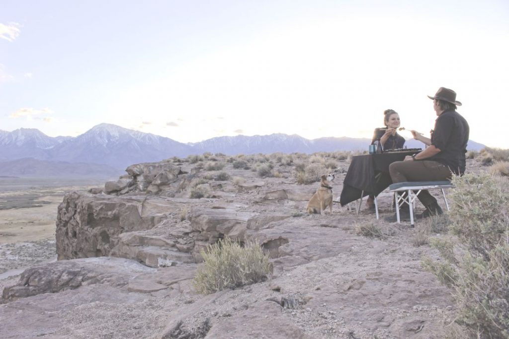 Andy and Ayana have their table and chairs set up in the middle of nowhere. Their dog is looking on